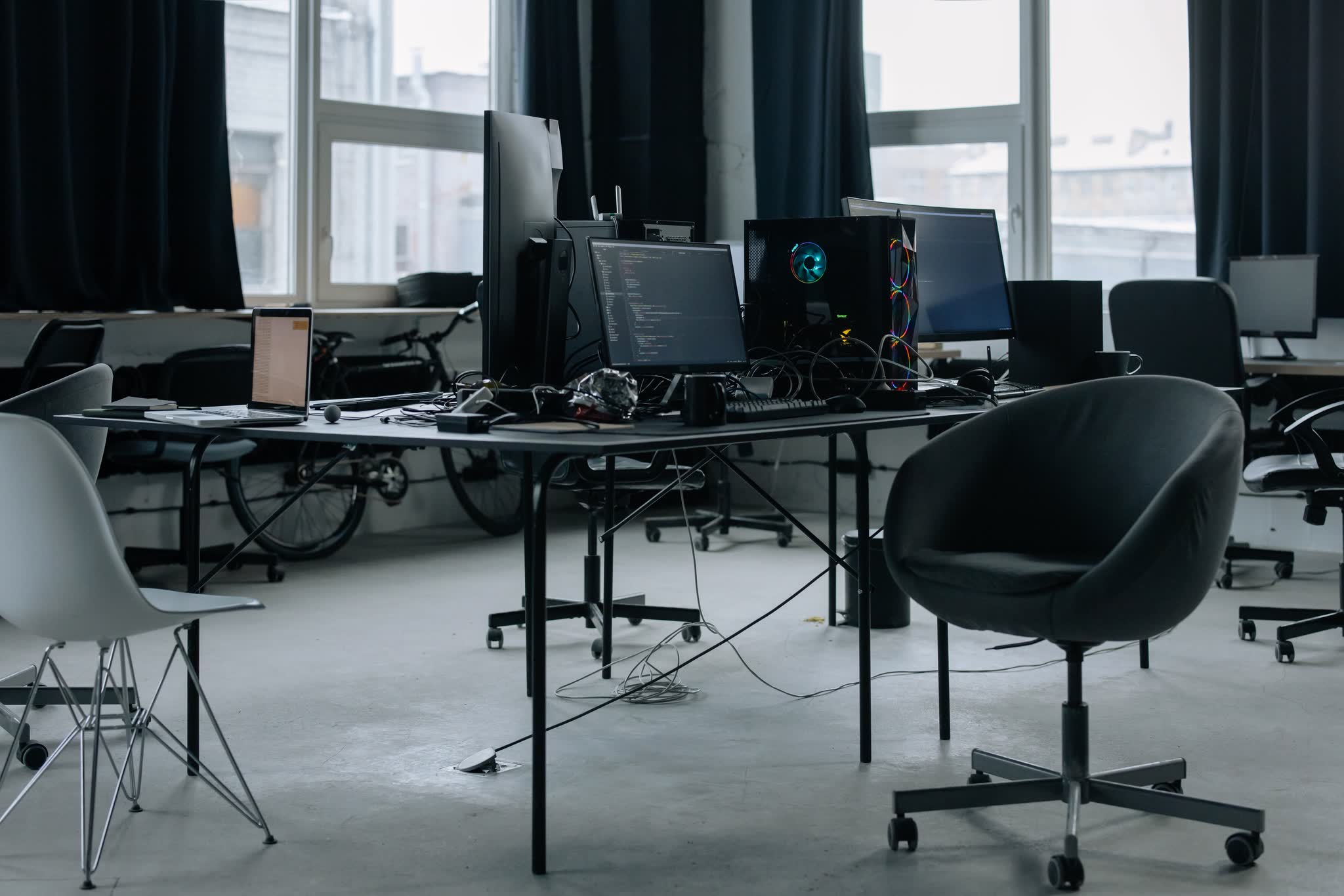 An empty workroom: desks, monitors and chairs under daylight.